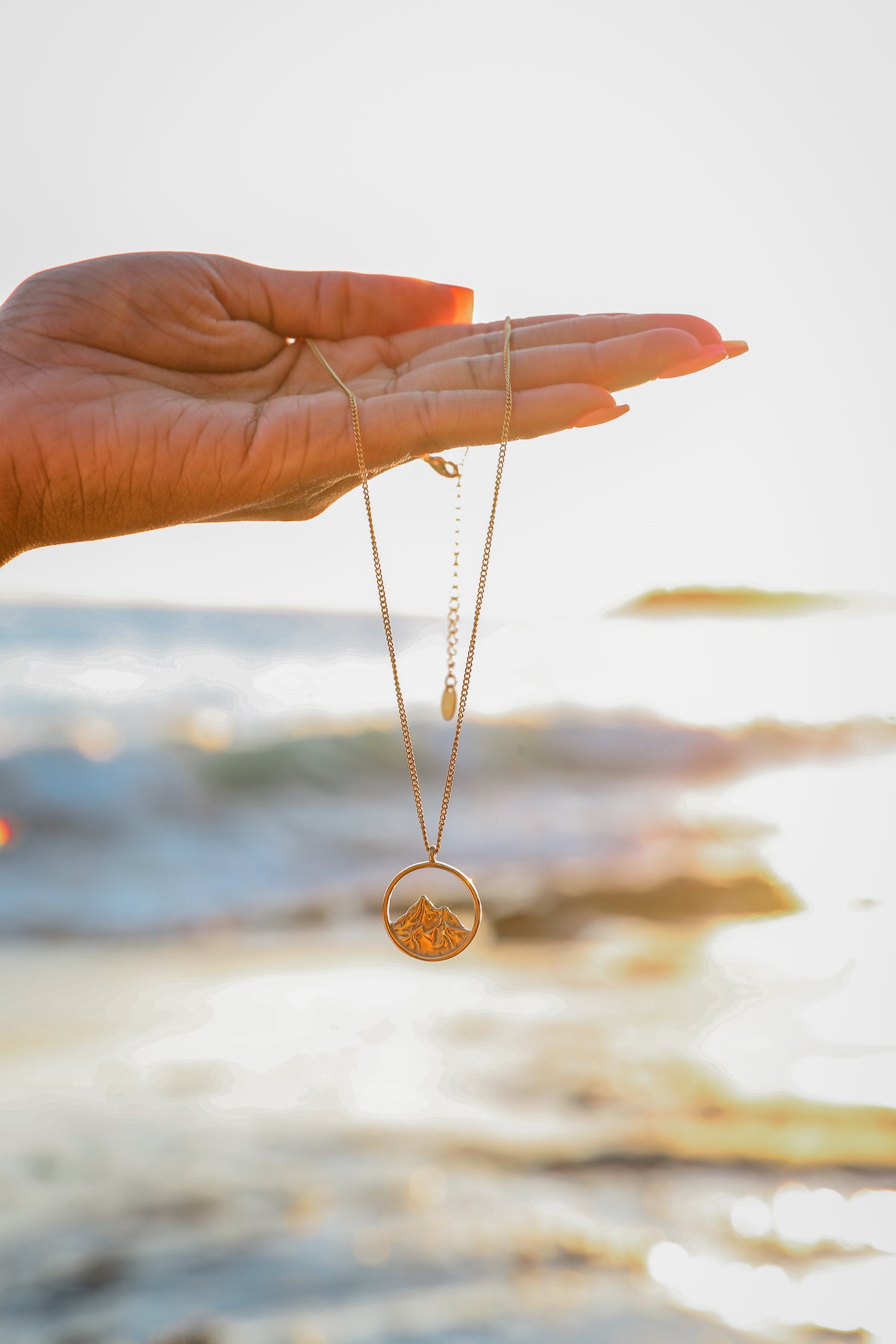 Breaking point necklace hanging from model hand with beach background