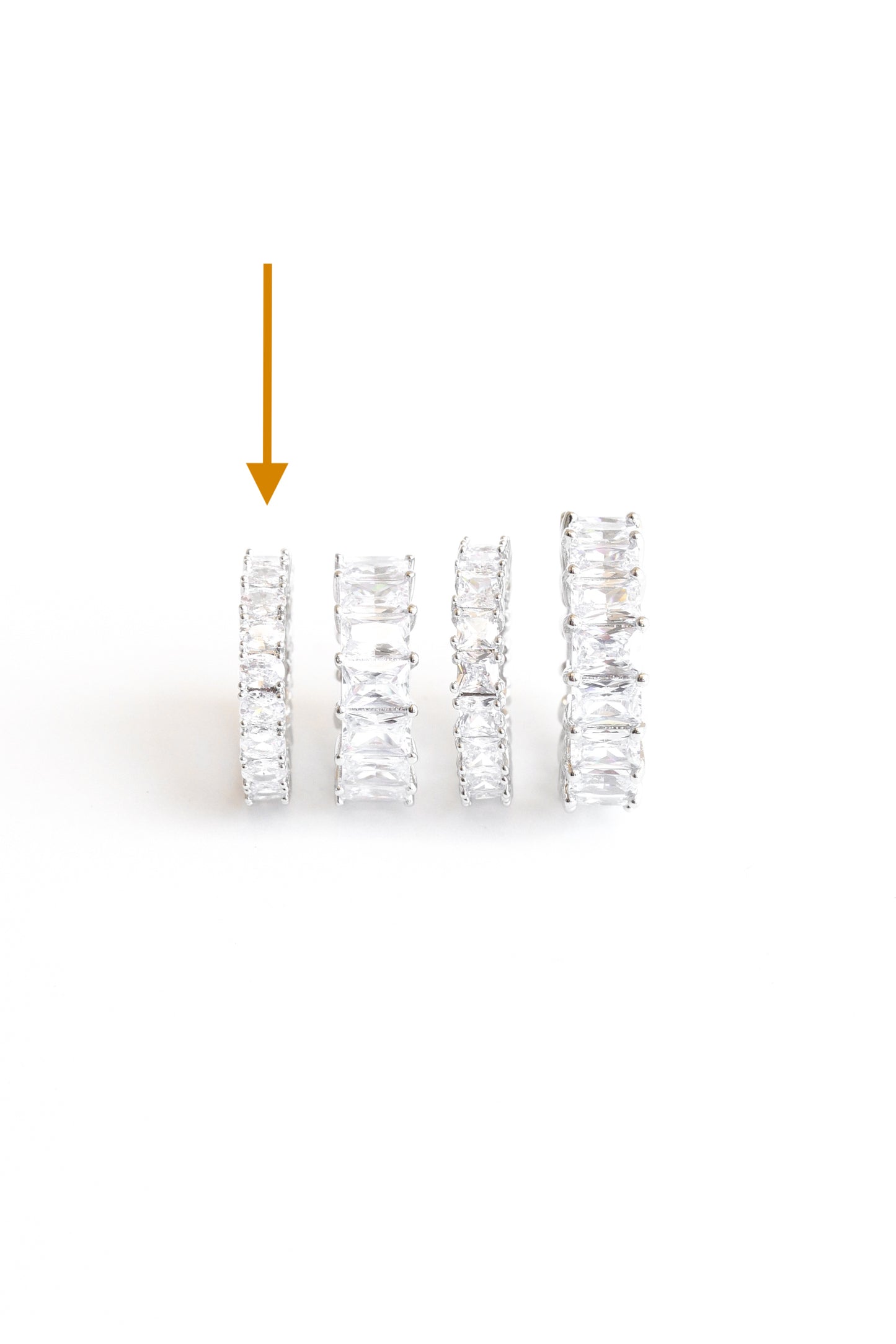 arrow pointing to Oval Amor band ring with other crystal rings against a white backdrop