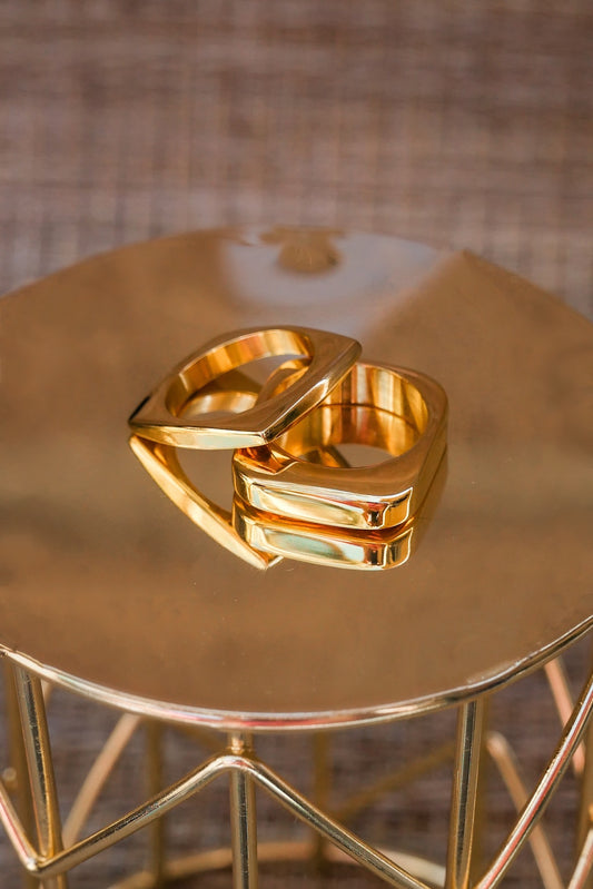  Two square gold out of the box rings on a gold table